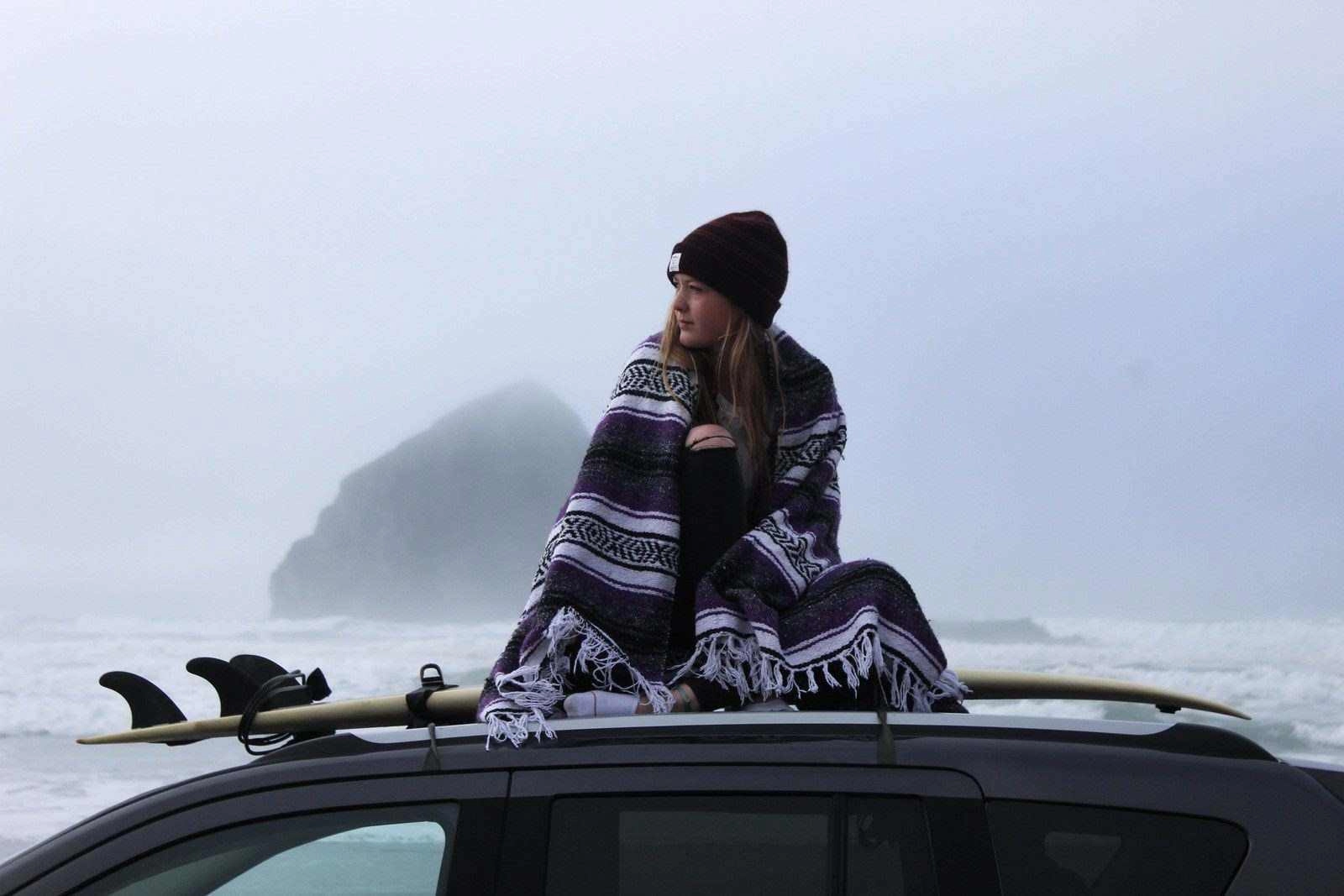 young-surfer-woman-sitting-on-a-car-roof-in-cannon-beach-united-states-importance-of-mental-health-when-traveling